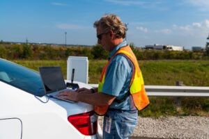 Man typing on laptop outside on the trunk of his car