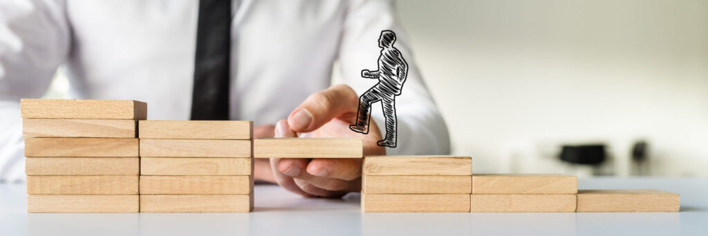 Wide view image of hand drawn shape of a businessman walking up the wooden steps supported by male hand. Conceptual of business teamwork and collaboration.