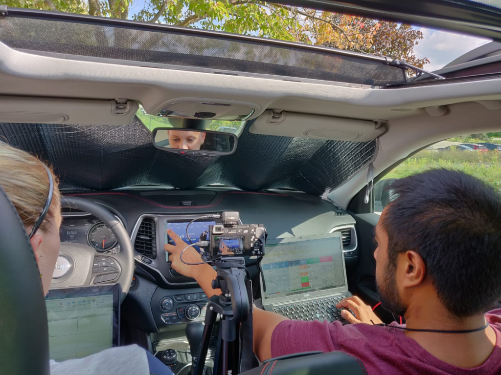 Man and women in car with camera on tripod and laptop