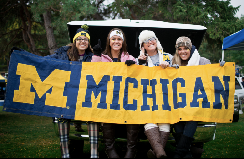 smaller version-four women tailgating and holding U-M sign