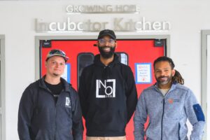 Eric Kinsler-Holloway of EK’s Cheesecakes and Brandon Frye of No Label Juice, both “graduates” of the Growing Hope Incubator Kitchen, with Growing Hope Executive Director Julius Buzzard. Doug Coombe